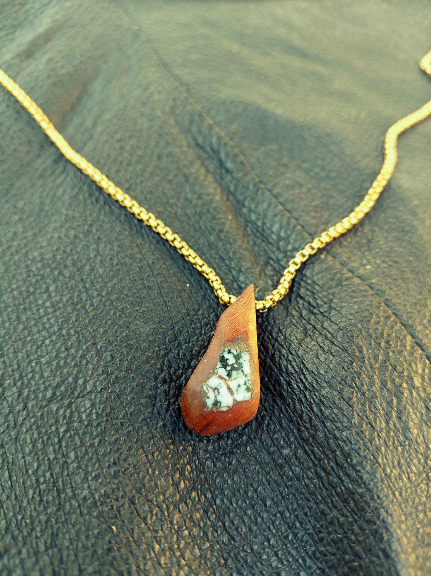 Wooden teardrop pendant with a speckled stone inlay on a gold chain