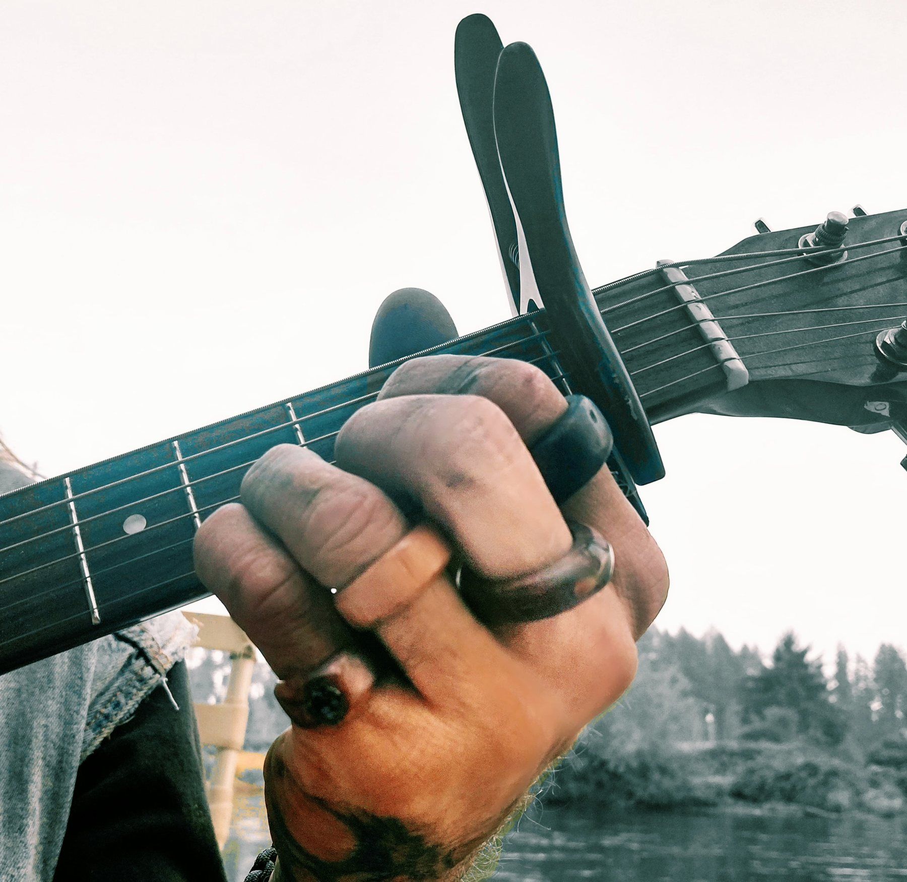 Four handmade wooden rings worn on one hand while playing guitar